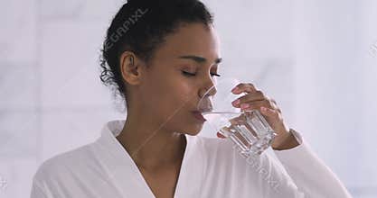 Beautiful healthy african woman drinking fresh mineral water in morning