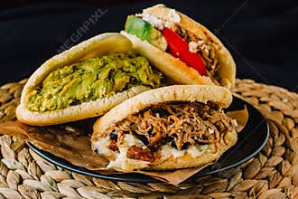 Venezuelan arepas on a black background, made with maize and filled with avocado, tomato, meat, cheese and black beans