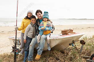 Family Sitting On Boat With Fishing Rod On Beach