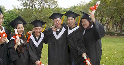 Happy  students in graduation gowns holding diplomas on university campus