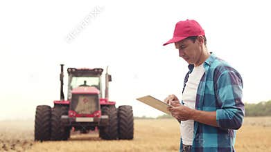 Agriculture. farmer working on a digital tablet in a field in the background a tractor plows ground in a field of wheat