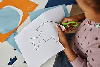Above shot of little girl cutting fish outline drawn on white paper