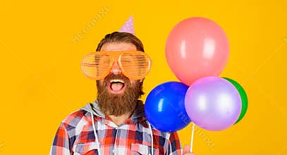 Happy bearded man in party glasses and birthday hat with balloons. Handsome guy celebrating birthday with multicolored