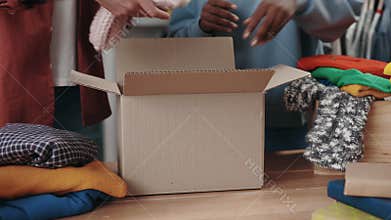 Multiracial volunteers selecting clothes for recycle or donating and putting it into the cupboard box at the charity