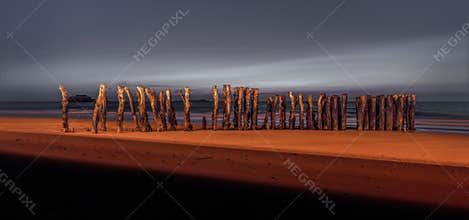 Saint Malo beach wooden pillars lit by the street lamps during the sunset