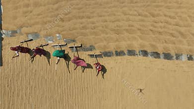 Aerial view of millions of grains of rice are laid out to dry at a mill as workers brush them with leaves in the hot sun.