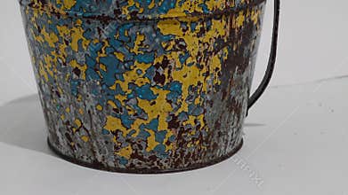 Metal bucket revealing weathered paint layers, rusty patina highlighting textural details against clean white backdrop