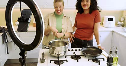 Two female hosts greeting viewers teaching recipe preparing carrots with ring light in home kitchen