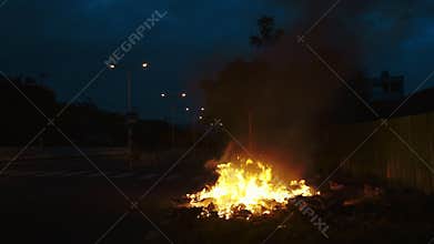 Large bonfire of unauthorized waste burns on roadside edge at night