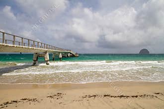Concrete pier stretching into vibrant turquoise ocean waters, with sandy beach waves and the distinctive Le Diamant rock on the