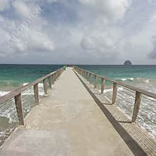 Long concrete pier stretching into the turquoise waters of the Caribbean Sea under an overcast sky, with the iconic Rocher du