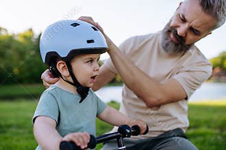 Father teaching toddler son to ride balance bike while wearing safety helmet.