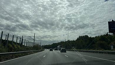 cars driving on a highway under an overcast sky with roadside trees