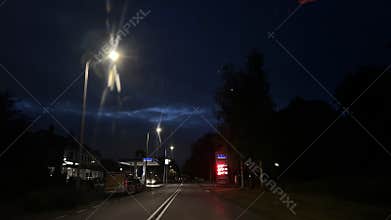 Night street with lit lampposts and gas station under deep blue sky