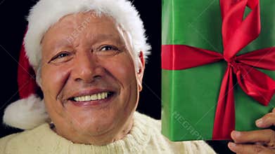 Merry Aged Man With Santa Hat Showing A Green Gift