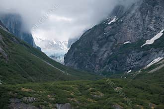 Grassy valley in Endicott Arm with lowering fog ,craggy mountains and icy glacier