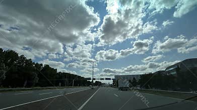 Highway traffic under cloudy sky with sun peeking through scattered cumulus