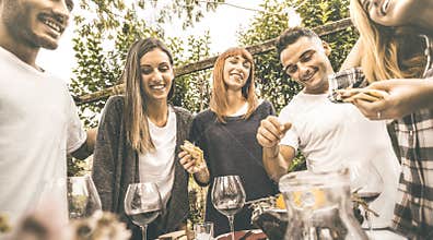 Happy friends having fun drinking red wine eating at garden party