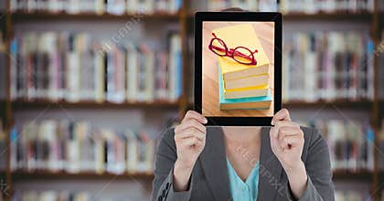 Business woman with tablet over her face with piles of books while standing at library