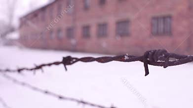 Close-up shot of old rusty barbed wire fence in former concentration camp. Brick barracks in the snow. 4K clip