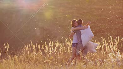 Young couple are madly having fun. A woman is beating her pillow with a friend, feathers are flying. Fight against the