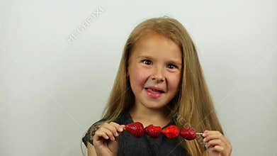 Beautiful girl taste strawberries on skewers. Smiling girl eats a strawberry licking lips.