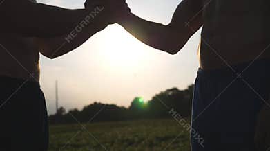 Friendly handshake of two unrecognizable muscular white men with sun shine at background. Shaking of male arms outdoor