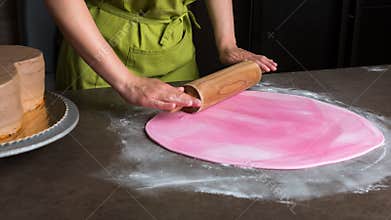 Woman using rolling pin preparing pink fondant for cake decorating