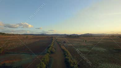 Narrow, African village dirt road with fields and farms in the background