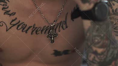 The cross hanging on the neck tattooed man
