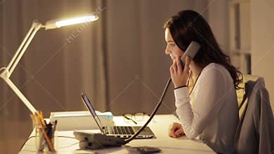 Woman with laptop calling on phone at night office