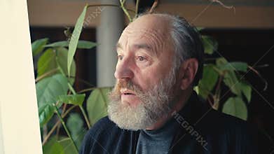 Lonely sad old man looking through the window and talking to himself 4K