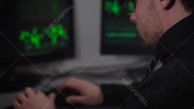 Close up of hacker sitting at the table with computer monitors and using keyboard to match password and gain