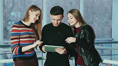The company of cheerful young people use a touch screen tablet gadget .