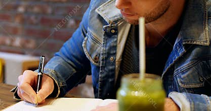Man writing in his dairy with juice on table