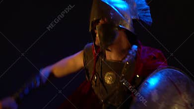 Roman Legionnaire in helmet and armor, falls into a rage, shields behind and beats sword, a bit slow motion