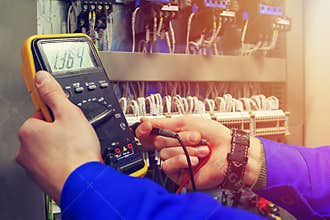 Multimeter in hands of electrician close-up against background of electrical wires and relays