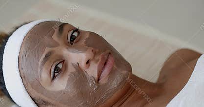Woman With Clay Facial Mask In Spa