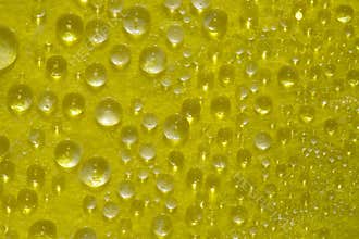 Illuminated by the bright sun transparent drops of water are located on a yellow glass surface.