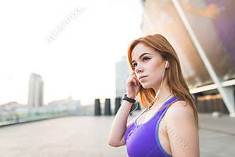 Attractive girl with a cup of coffee in her hands, wearing a beige coat, standing against the wall with windows and looking to the