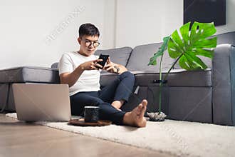 Young Asian man working from home and chatting with smartphone after working by using laptop computer. Work from home concept