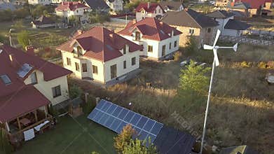 Aerial view of a residential private house with solar panels on roof and wind generator turbine.