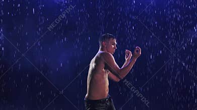 Sexy young man in wet jeans emotionally dancing modern ballet dance in the rain. Contemporary choreography on a smoky