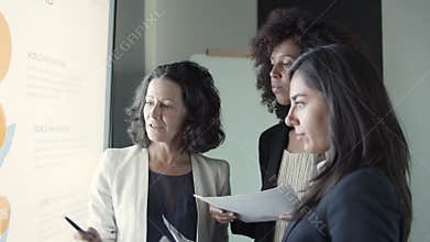 Three businesswomen holding documents and discussing project