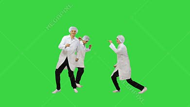 Three male doctors in white robes and protective caps running in the frame and start doing funny dance on a Green Screen