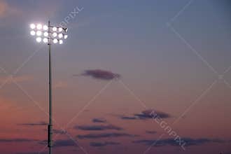 Stadium night lights over football field during sunset with cumulous clouds