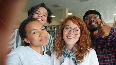 Multi-racial group of young people taking selfie in college library smiling