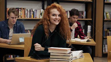 Portrait of a young red headed curly female student working on her thesis or preparing for exam. Reading a book sitting