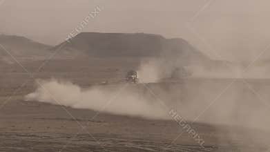Military soldiers moving through the desert, driving a truck, raising clouds of dust.