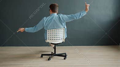 Smiling guy spinning on office chair pointing at camera on dark gray background